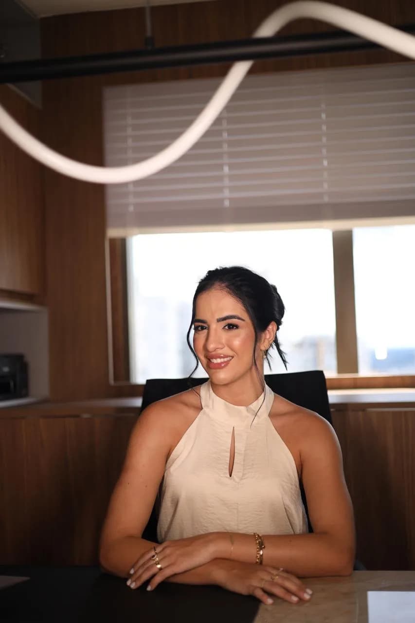 Dra. Yanka Fernandes sentada à mesa do consultório, sorrindo para a câmera