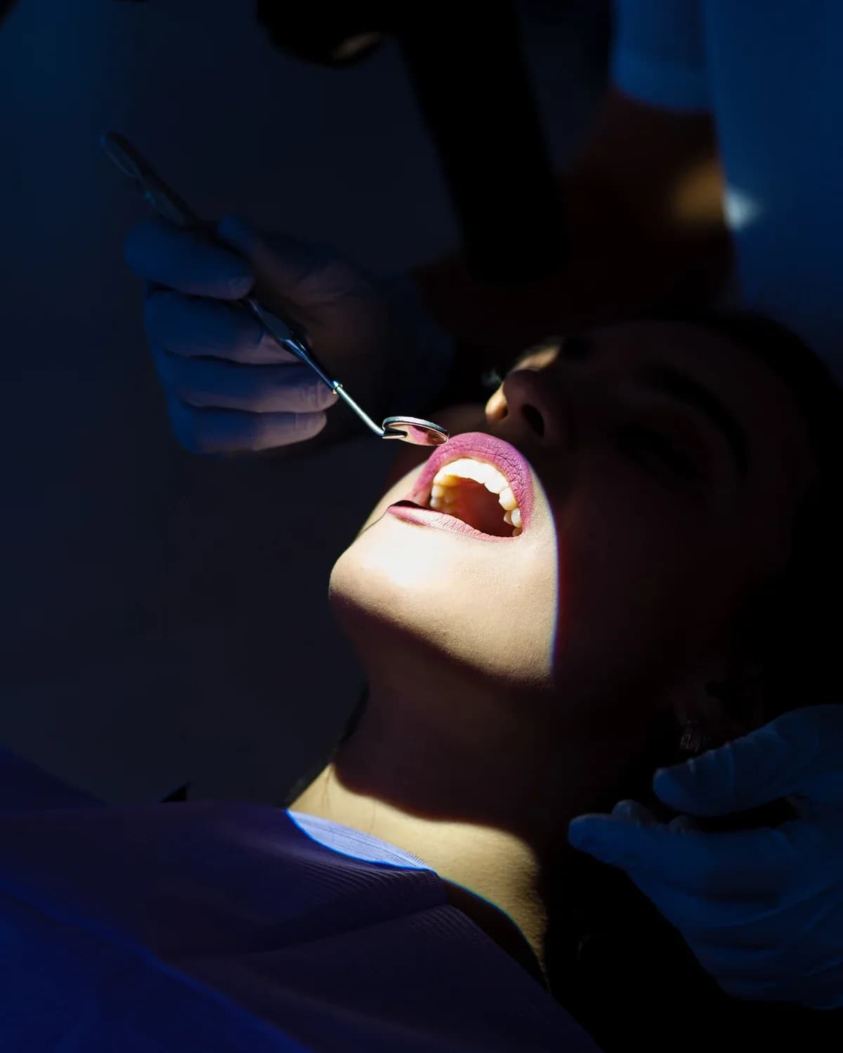 Paciente reclinada durante exame do dente, com espelho clínico em uso